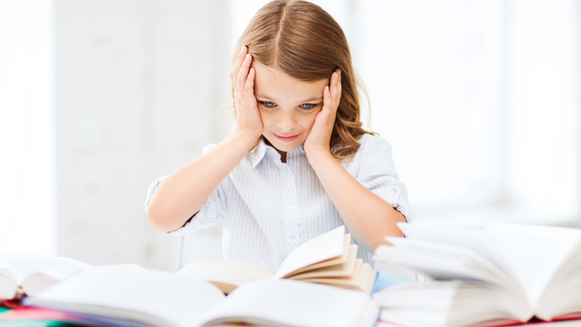 Image of a child sitting at a table full of books, reading and holding its head